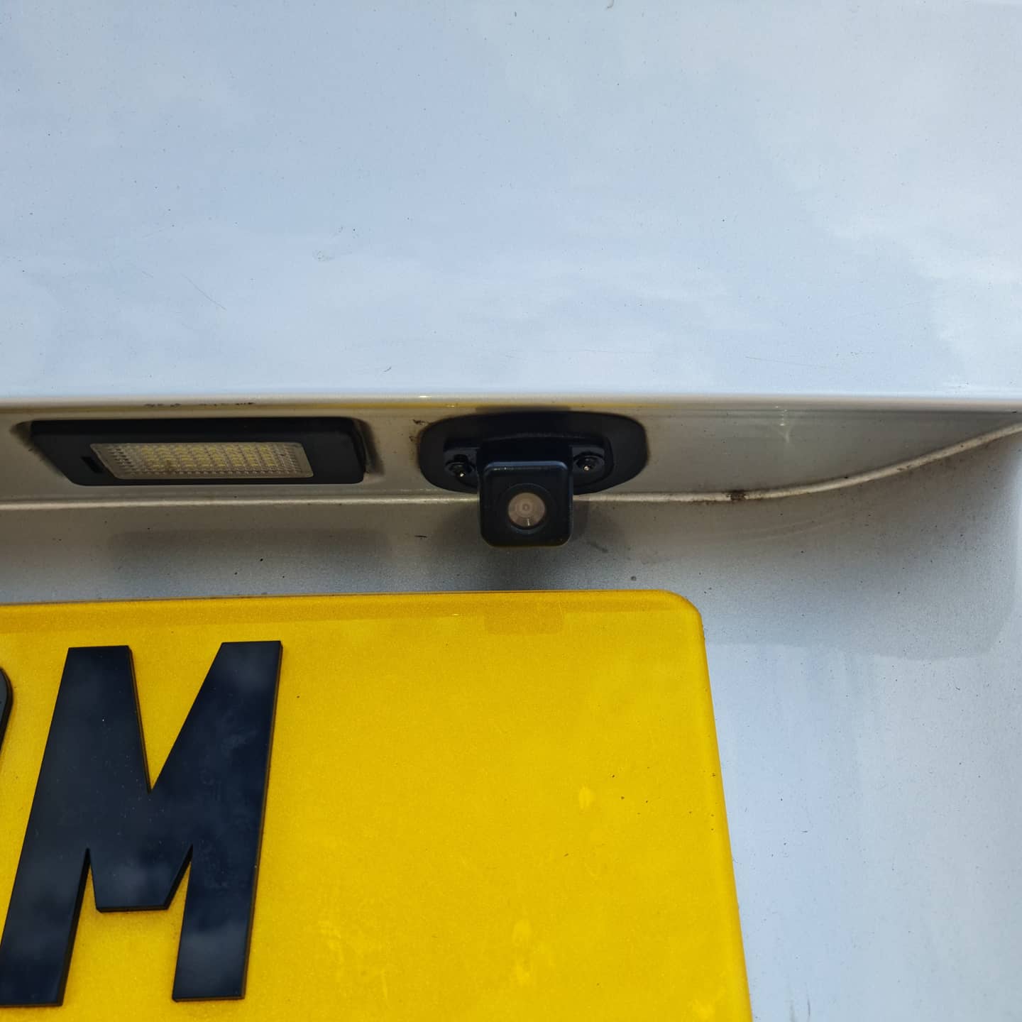 A reverse camera mounted above a yellow number plate on a white tailgate