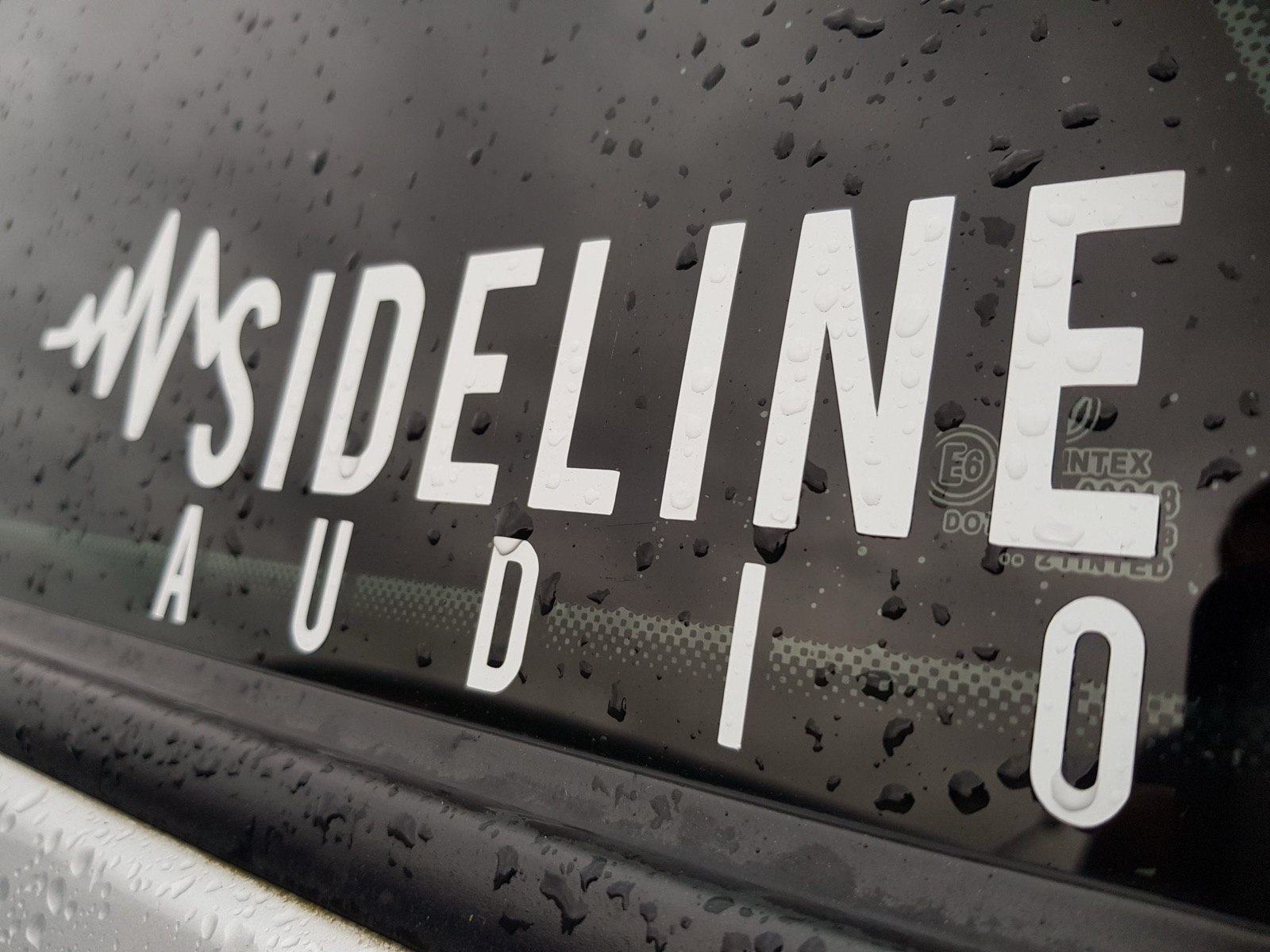 A white Sideline Audio decal on a wet car window