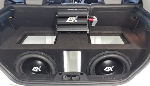 Twin ESX subwoofers in a carpeted enclosure with an ESX amplifier racked above them in a car boot