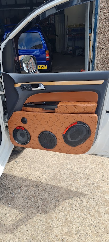 A custom door card trimmed in tan quilted leather with three speakers fitted, door open in the workshop